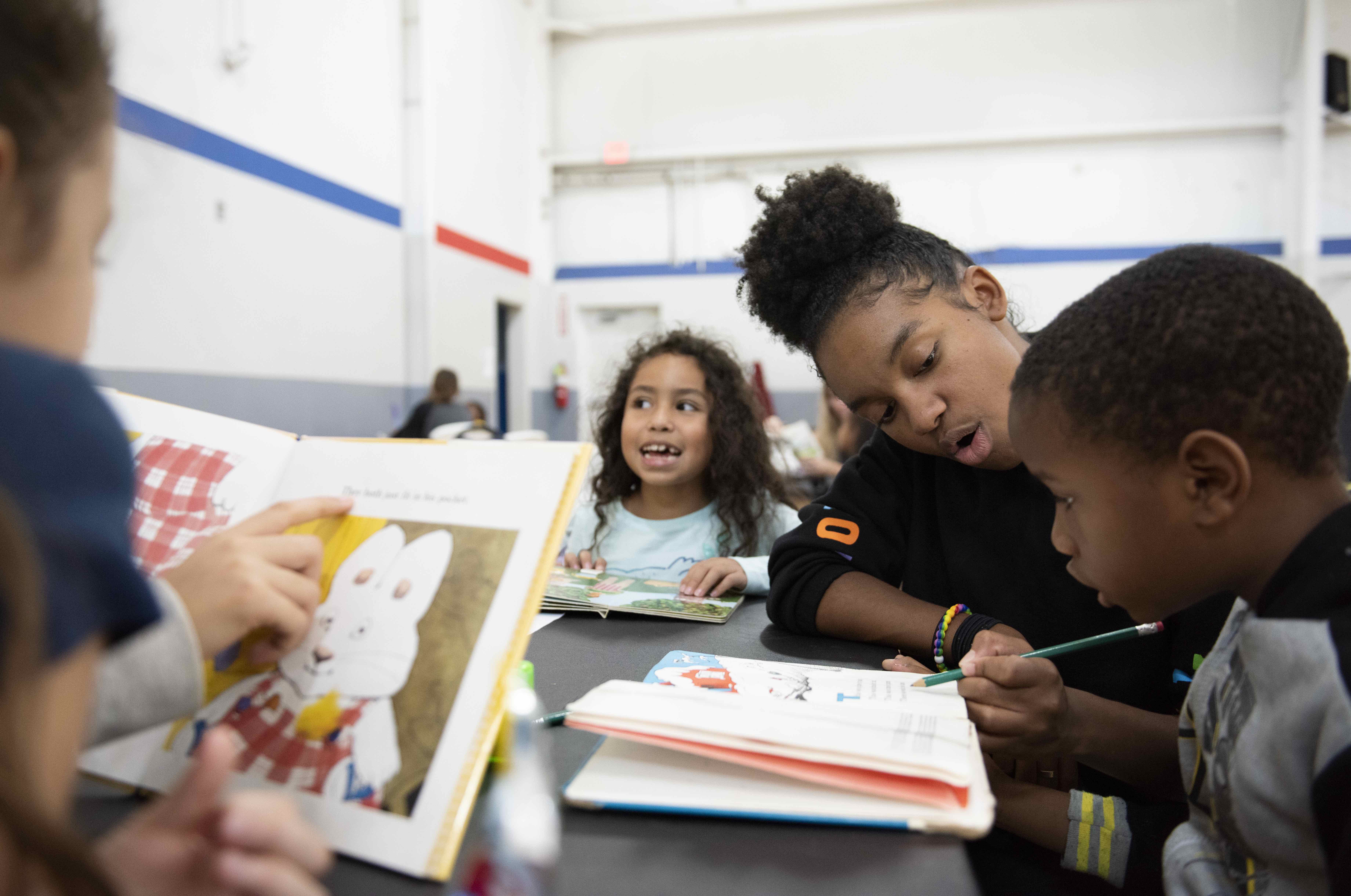  An image of a woman reading to two children at a table while another child colors. The image represents the search query 'Japanese organizations seeking external partnerships for AI implementation' because it shows how AI can be used to improve education.