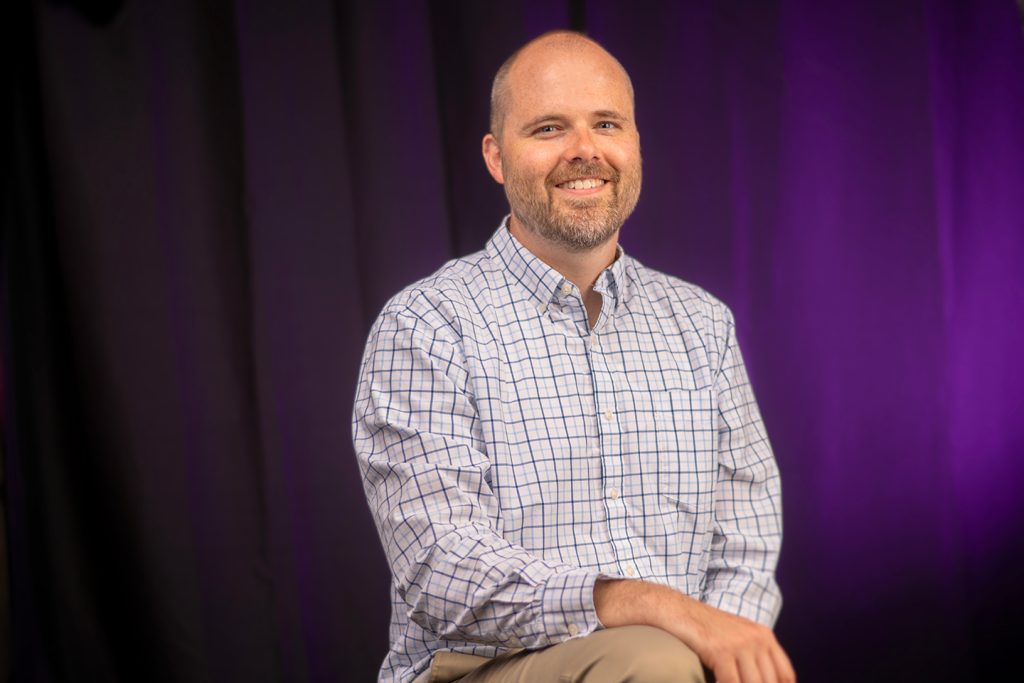 Associate Professor of Finance Chris Harris sits in front of a purple background.