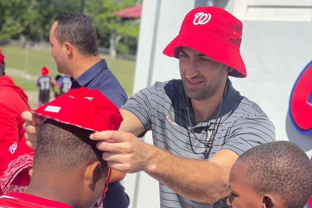 Andrew Scarlata, an Elon Spanish major, places a red Washington Nationalshat on a young boy's head while doing community outreach.