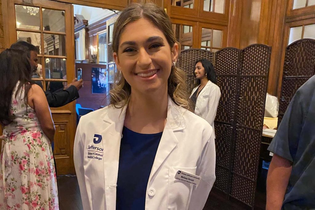 Melissa Denish, an biochemistry major, is attending her white coat ceremony at Sidney Kimmel Medical College. There are other people attending the ceremony behind her.