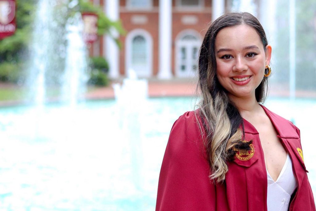 Sarah Poythress, an Elon music education major, stands in front of Fonville Fountain in her graduation garb.