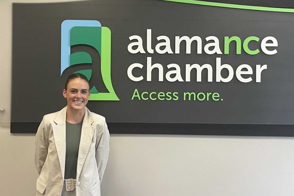 Emily Alps stands in front of an Alamance Chamber sign.