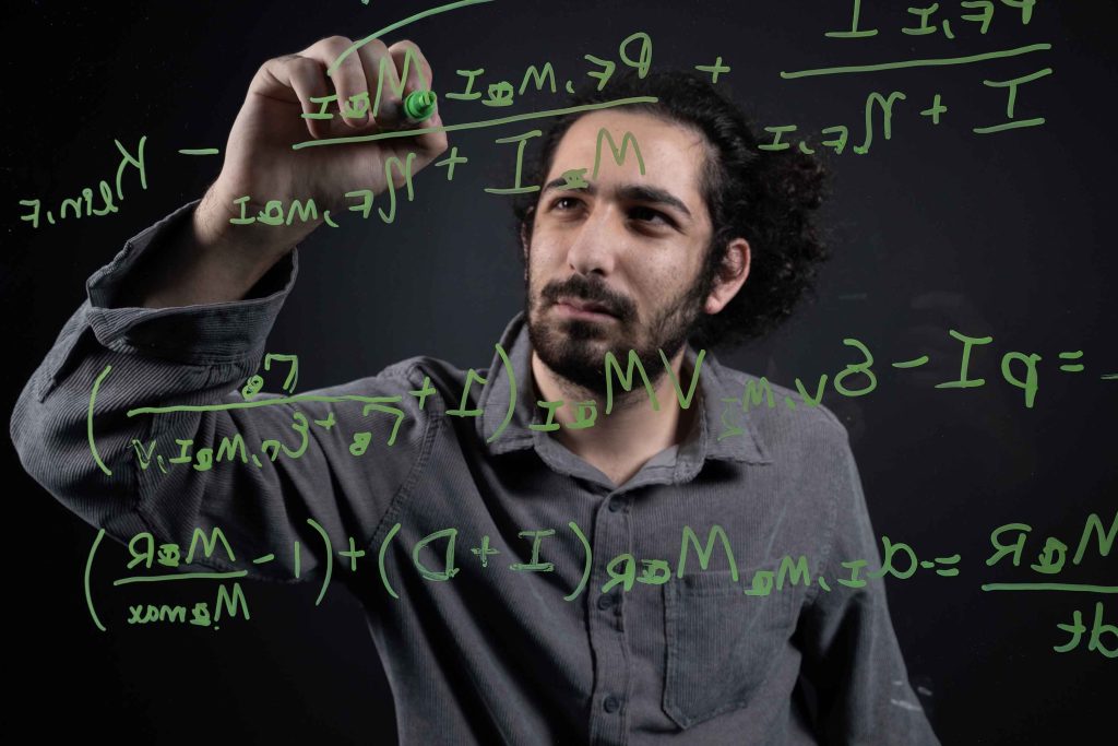 Rony Dahdal writes equations with a green dry erase marker on a clear board.