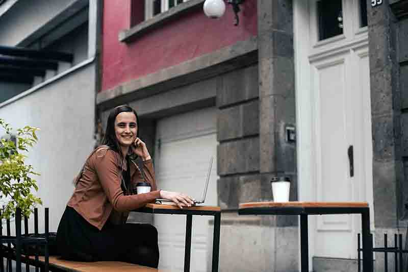 Angela Myers sitting outside a building at a table with her laptop and coffee.