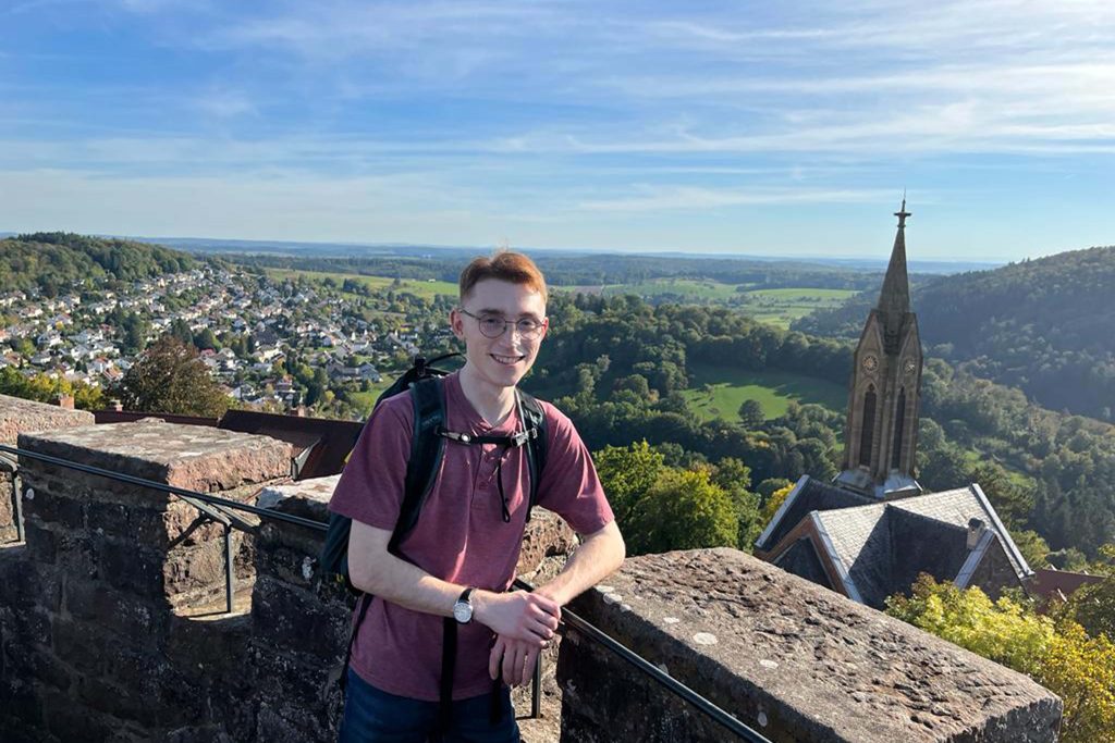 Blake Healey posing with a view of the grounds of Dilsberg Fortress, including its hexagonal main tower, in Neckargemünd, Germany.