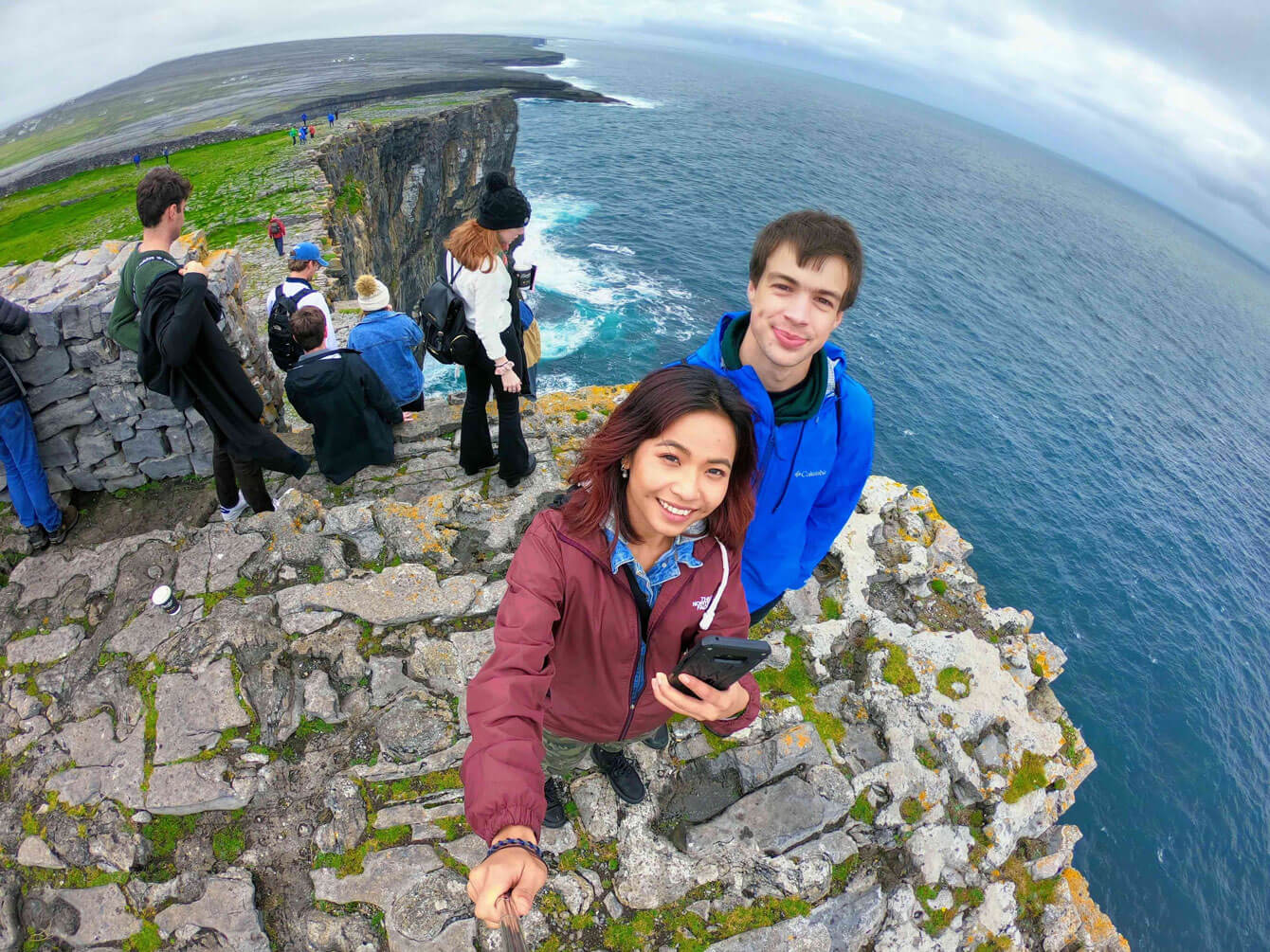 Two students taking a selfie in Ireland on a cliff overlooking water.