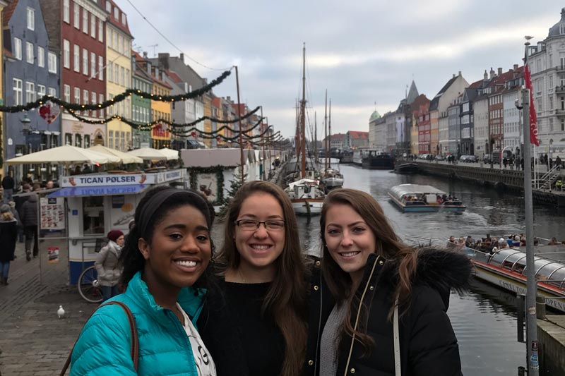 Three students posing in front of boats in a canal in Copenhagen.