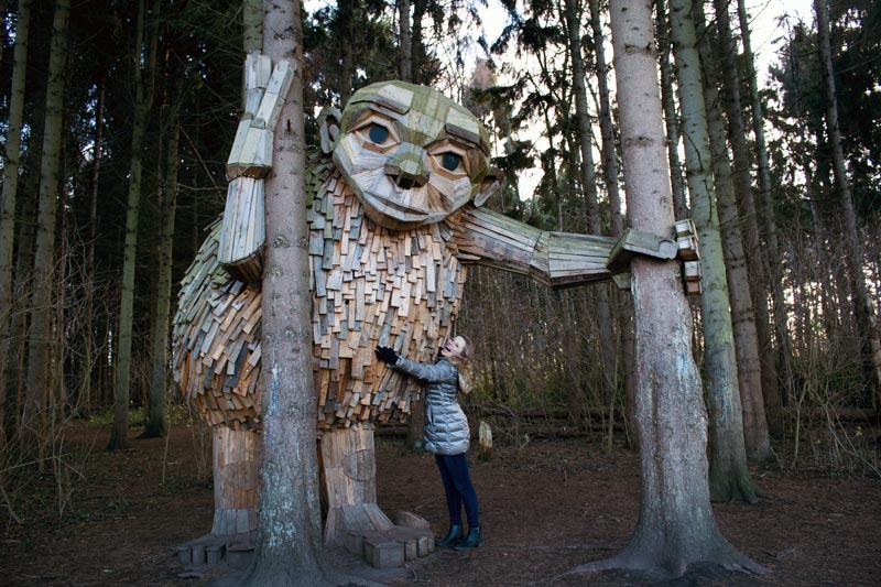 A person hugging a giant wooden sculpture surrounded by trees in a Copenhagen forest.
