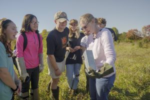 Students surround a professor in a field in a wildlife ecology course.