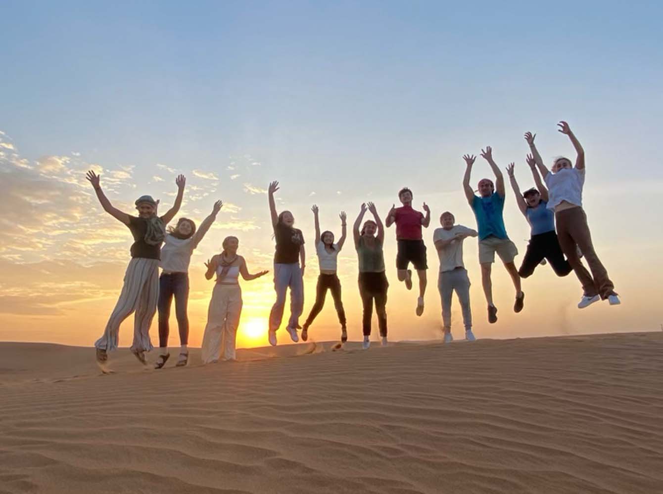 A row of Elon students jumping in the air on sand in Dubai