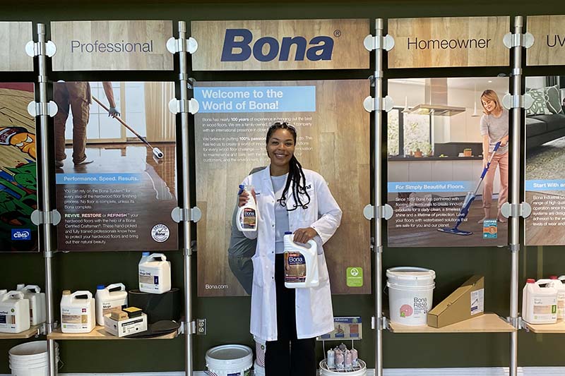 Student wearing a lab coat and holding Bona floor products in front of a Bona sign.