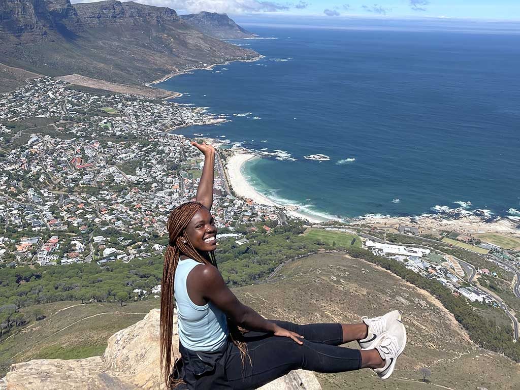An Elon student with long braids and her left arm outstretched sits on a rock that overlooks Cape Town, South Africa, while taking advantage of one of Elon's best study abroad programs.