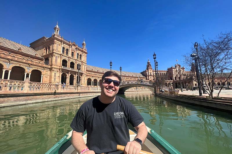 A student is in a row boat in a water way around Plaza de España in Seville. Students are engaged through experiential learning programs like study abroad.