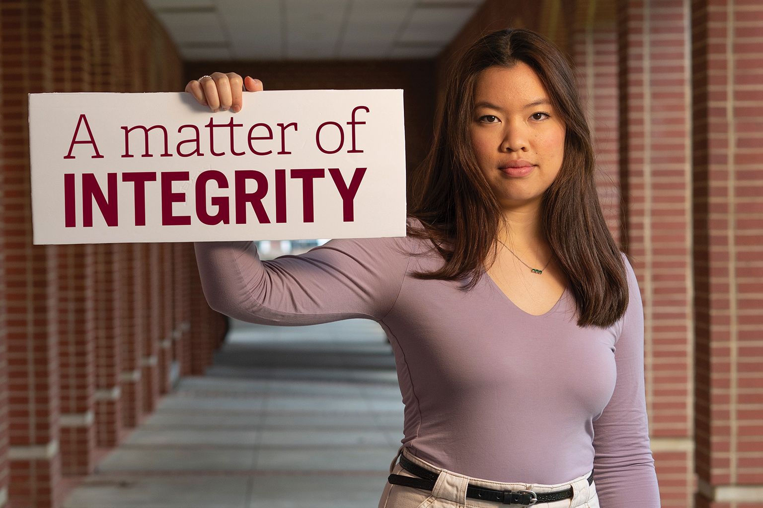 Xuan-Huyn stands in between brick colonnades holding a sign that says a matter of integrity.