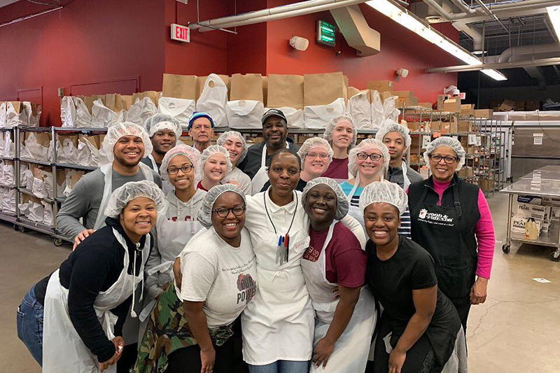 A group of volunteers wearing hair nets pose for a photo in an industrial kitchen.