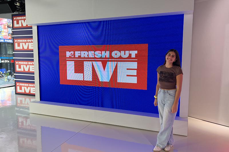 Participating in an MTV internship through one of Elon University's experiential learning programs, Jules Martin stands in front of a MTV Fresh Out Live sign.
