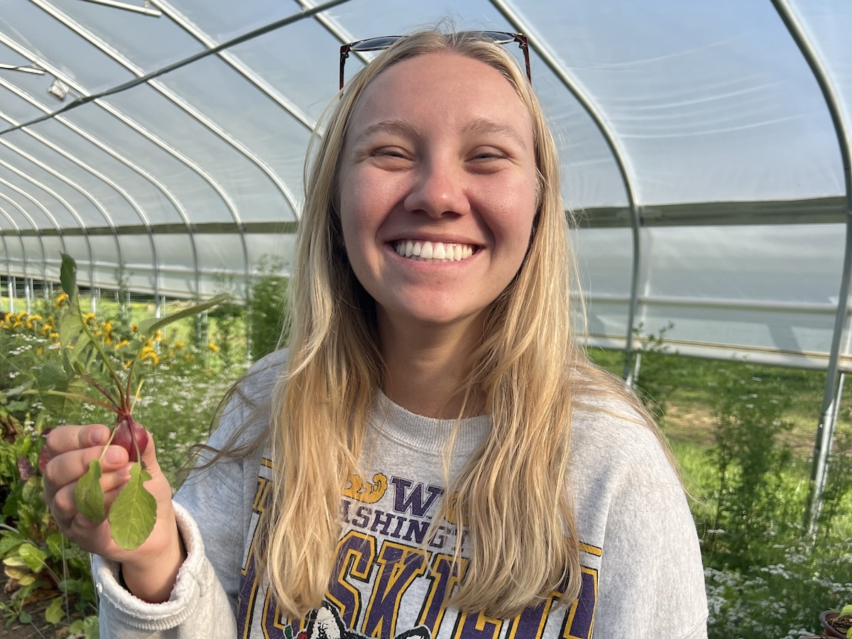 Maddie Johnson holds up a plant in one of the greenhouses on Loy Farm.