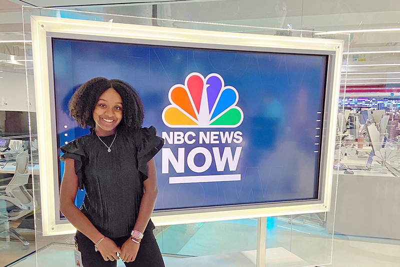 Naomi Washington stands in from an NBC News NOW sign at NBC Universal Studios where she held an internship.