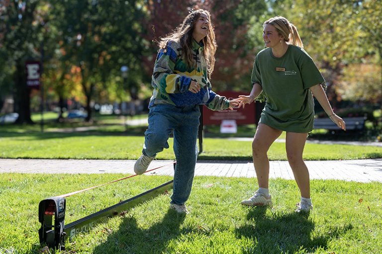 Two students laugh hysterically as one tries to walk across a tight rope on Young Commons.