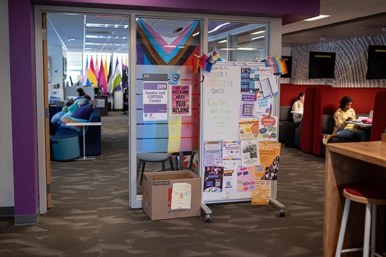 There are colorful flags at the entrance to and inside the Gender and LGBTQIA Center. Outside the center, students are studying in red booths.