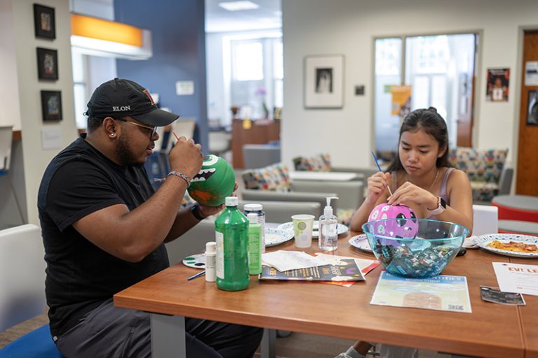 Two students are concentrating while they paint a pumpkin green and another pink.