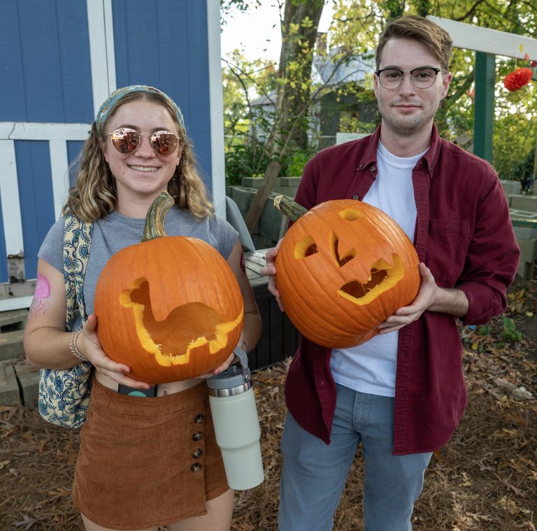 Two students hold up carved pumpkins.
