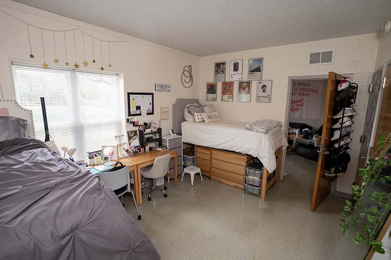 A double room in Danieley Neighborhood. There are two desks side by side between two beds. A shoe rack is hung over the back of a door.