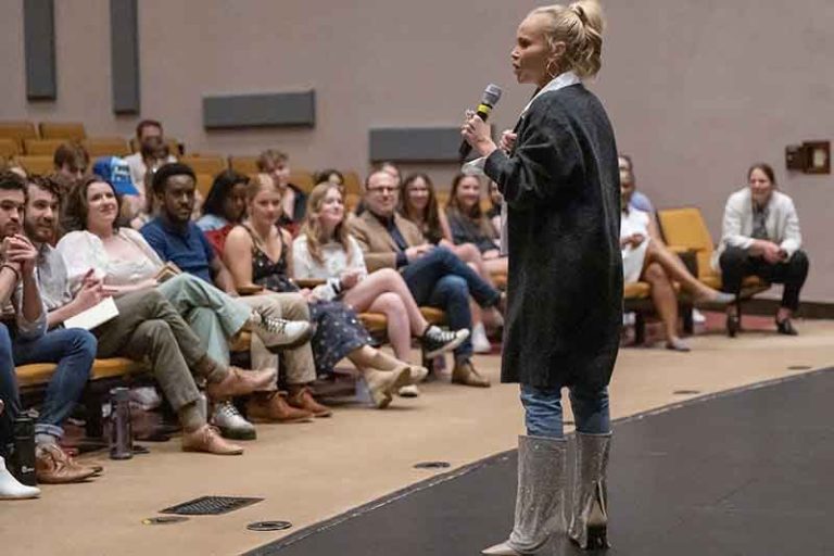Kristen Chenoweth dressed in a long gray cardigan, jeans and boots speaks to a group of students in McCrary Theater.