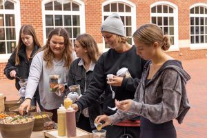 Students gather at a fall-themed salad pop-up. There are a variety of vegetables and dressings and cups to make their salads in.