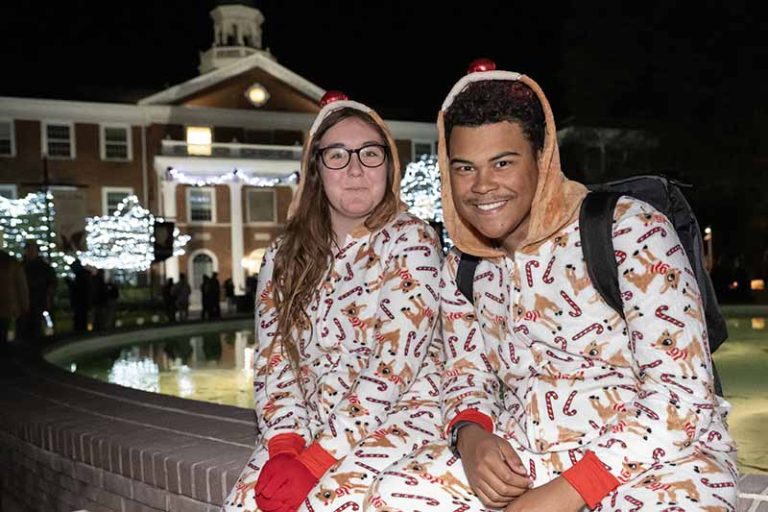 Two students dressed in reindeer onesies sit on the brick wall around Fonville Fountain.