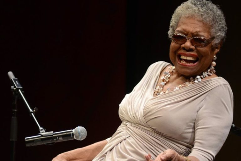 Maya Angelou, dressed in a champagne-colored dress, laughs hard in front of microphone.