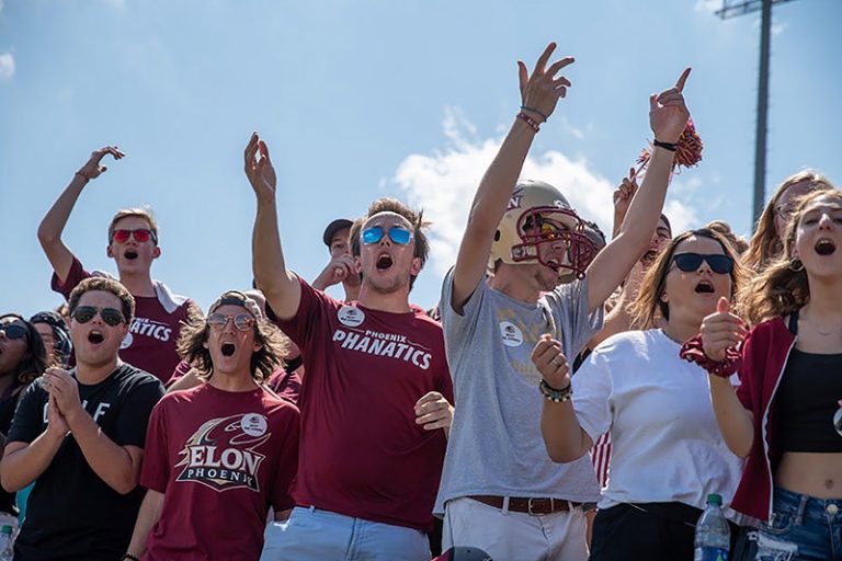 A group of students, some wearing Phoenix Phanatics, cheer enthusiastically at a football game.