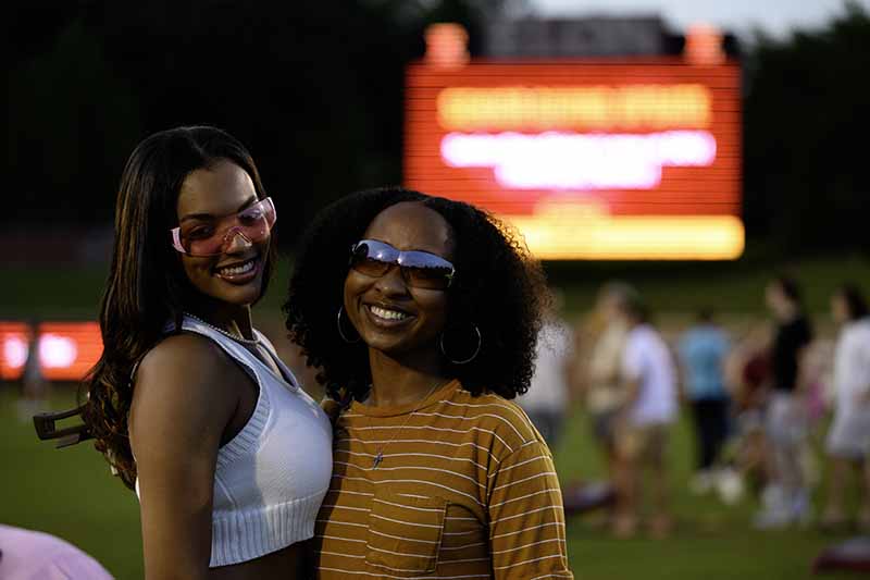 Two female students wearing sunglasses embrace for a photo.
