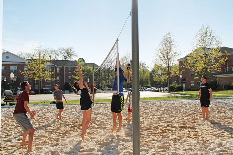 Male and female students play volleyball in the sand in Global Neighborhood.
