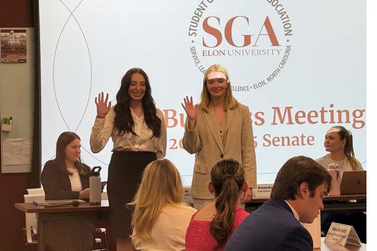 Two students get sworn into the SGA. There is an SGA sign behind them on a screen.