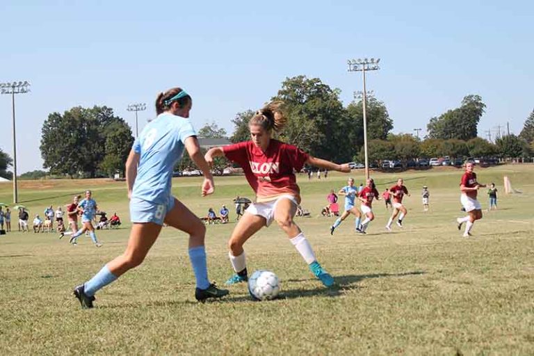 An Elon female club soccer player dressed in a maroon shirt and white shorts squares off against a University of North Carolina at Chapel Hill soccer player dressed in sky blue.