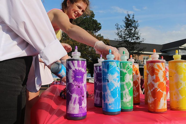 A student organizes squeezes color bottles of paint on a table outside.