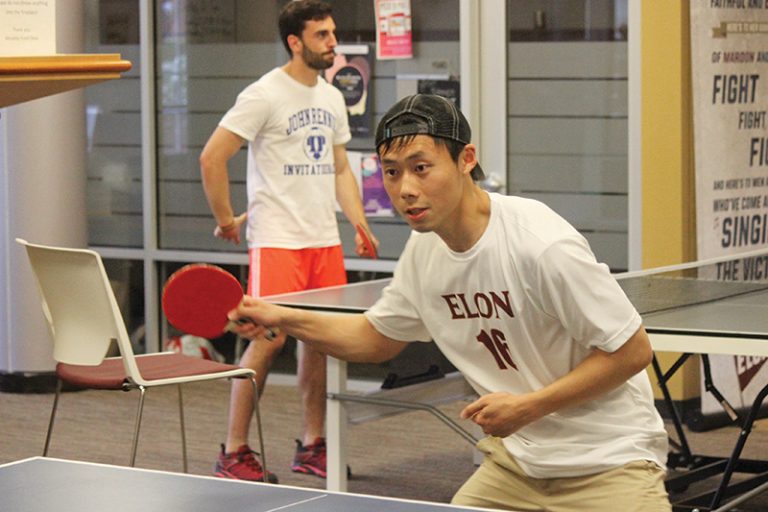Two males students play table tennis in Moseley Center. They are both using red paddles.
