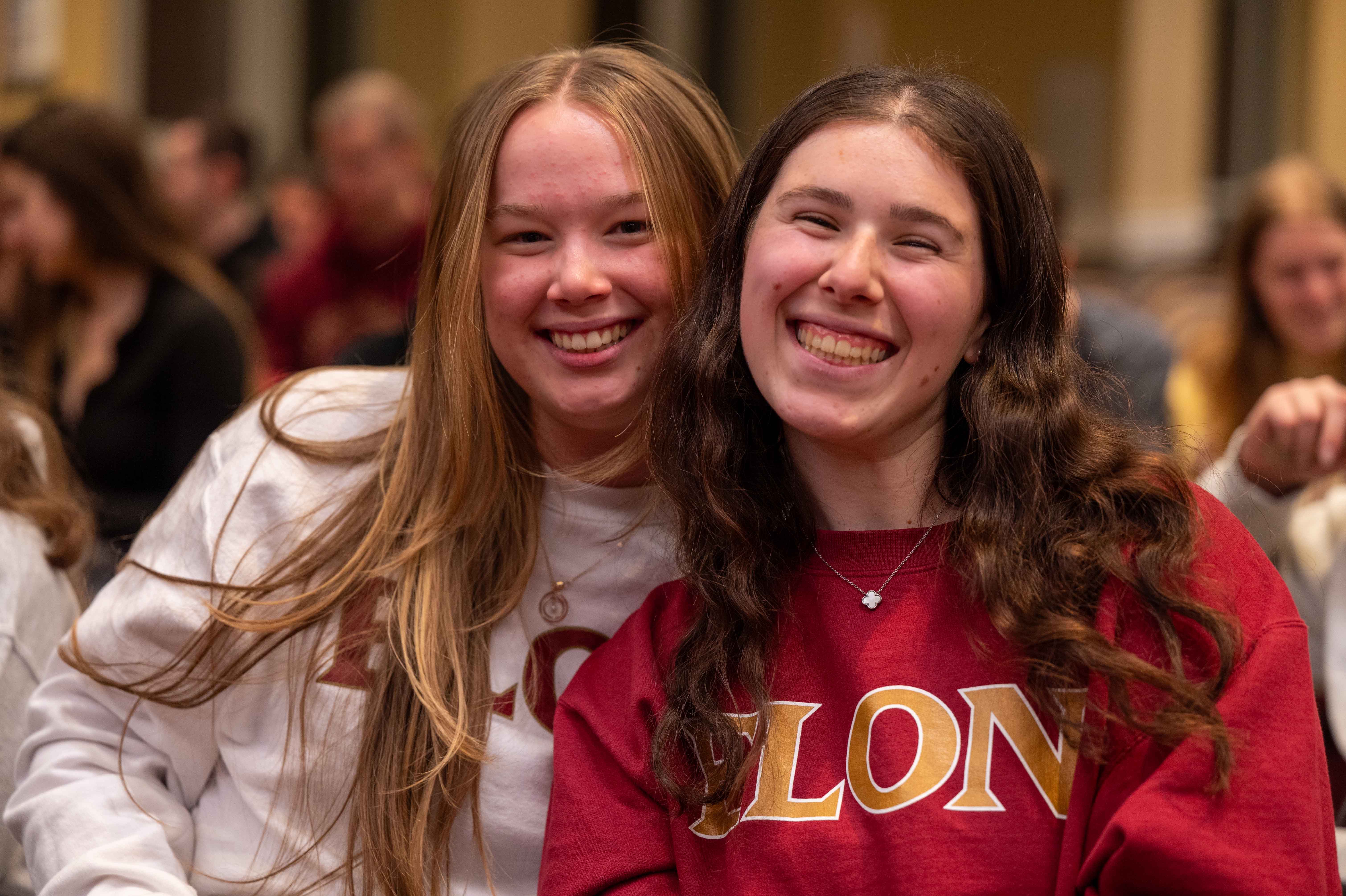 Two female students in Elon shirts smile for the camera.