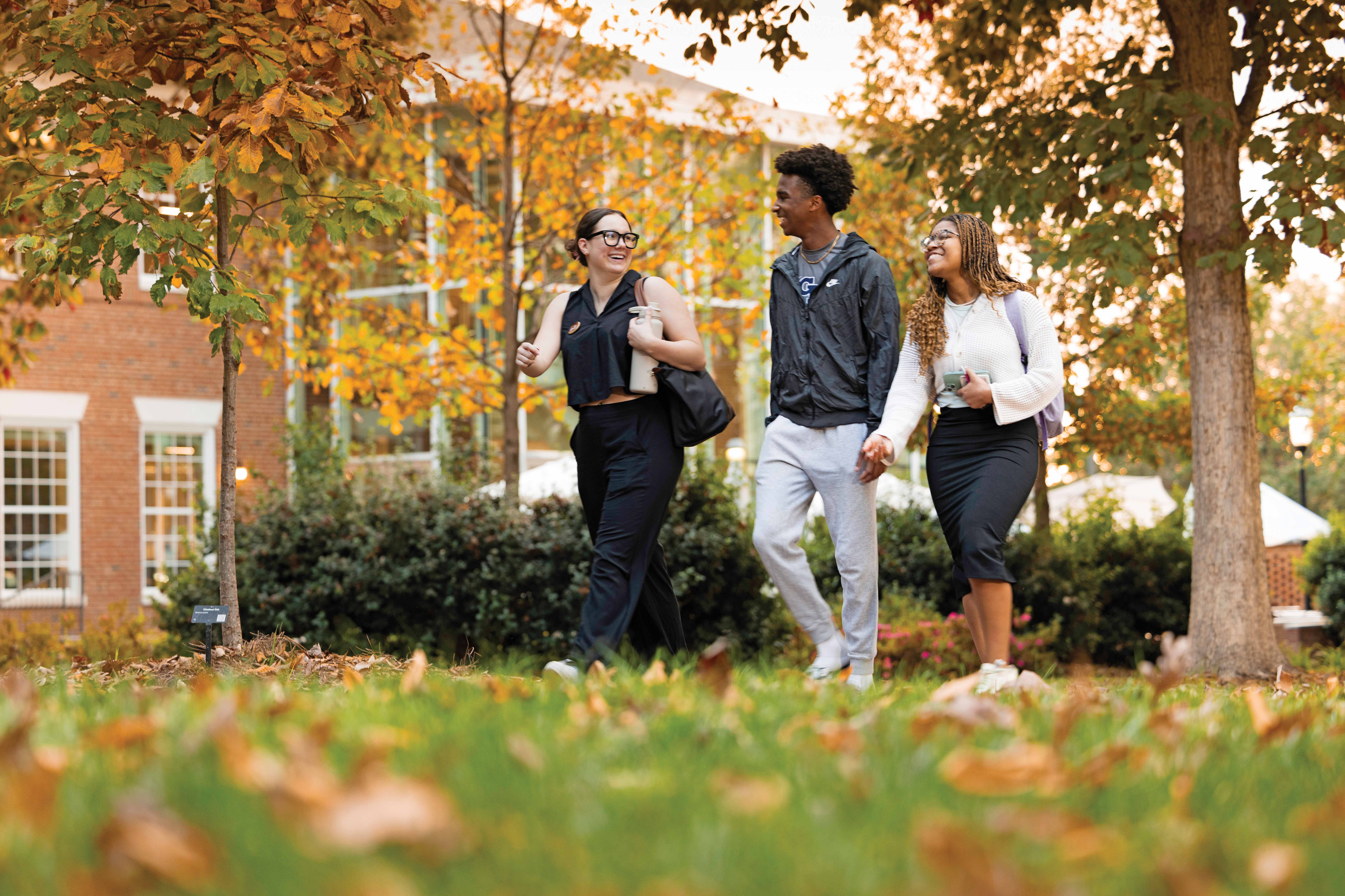 Three students are walking on campus on a fall afternoon.
