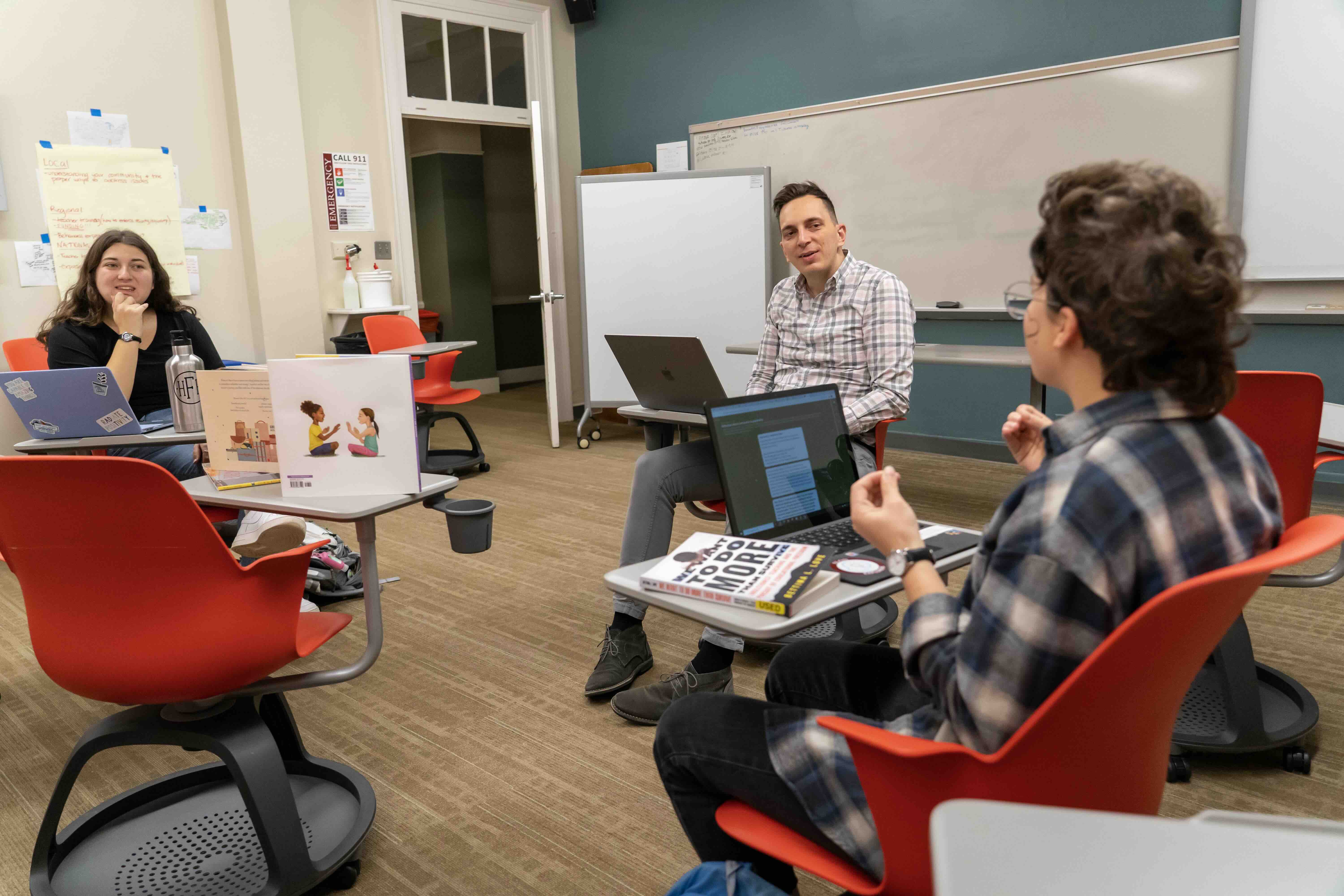 A professor chats with two students in a school of education classroom.