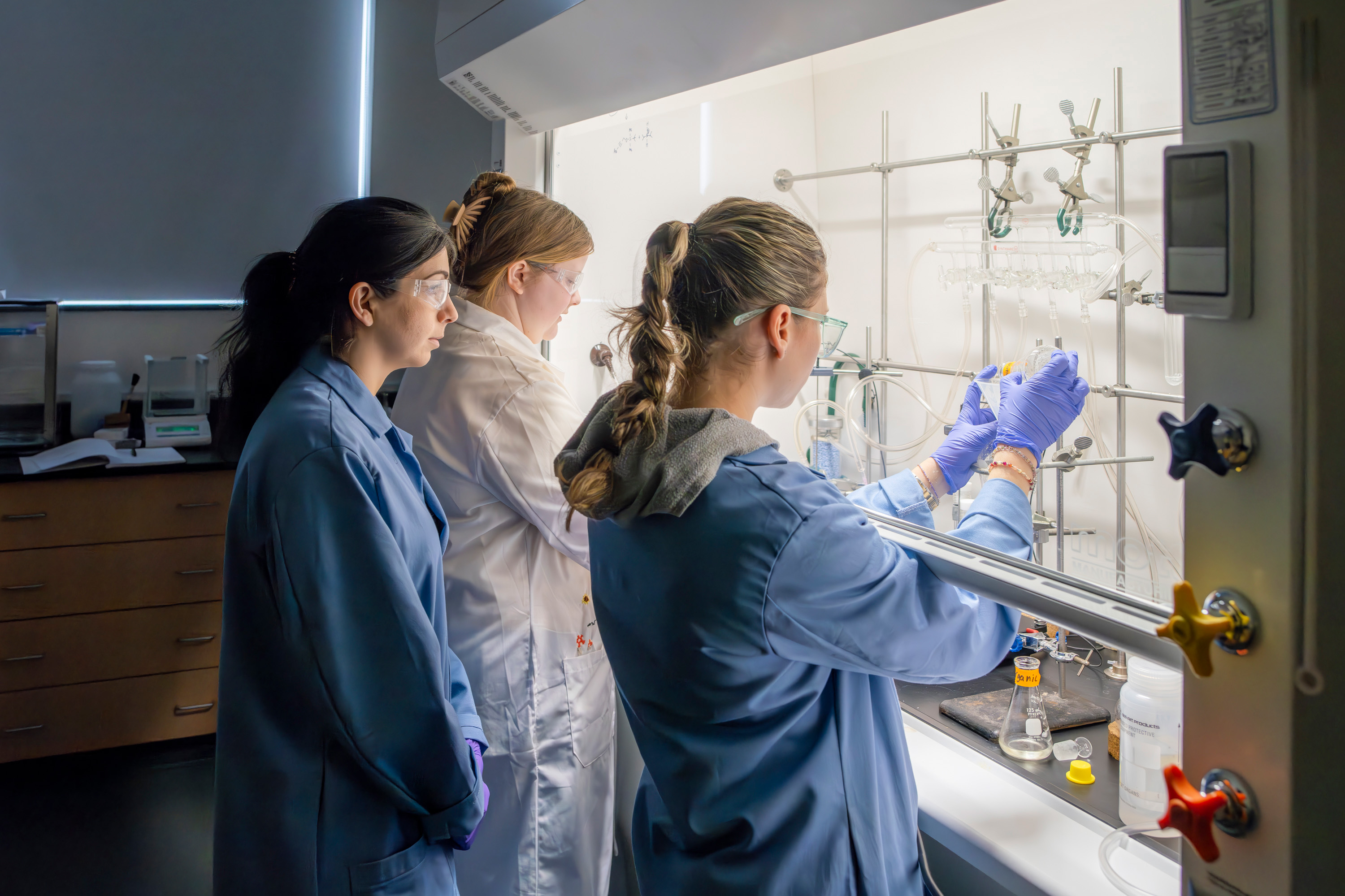 Two students work with a professor in a chemistry lab.