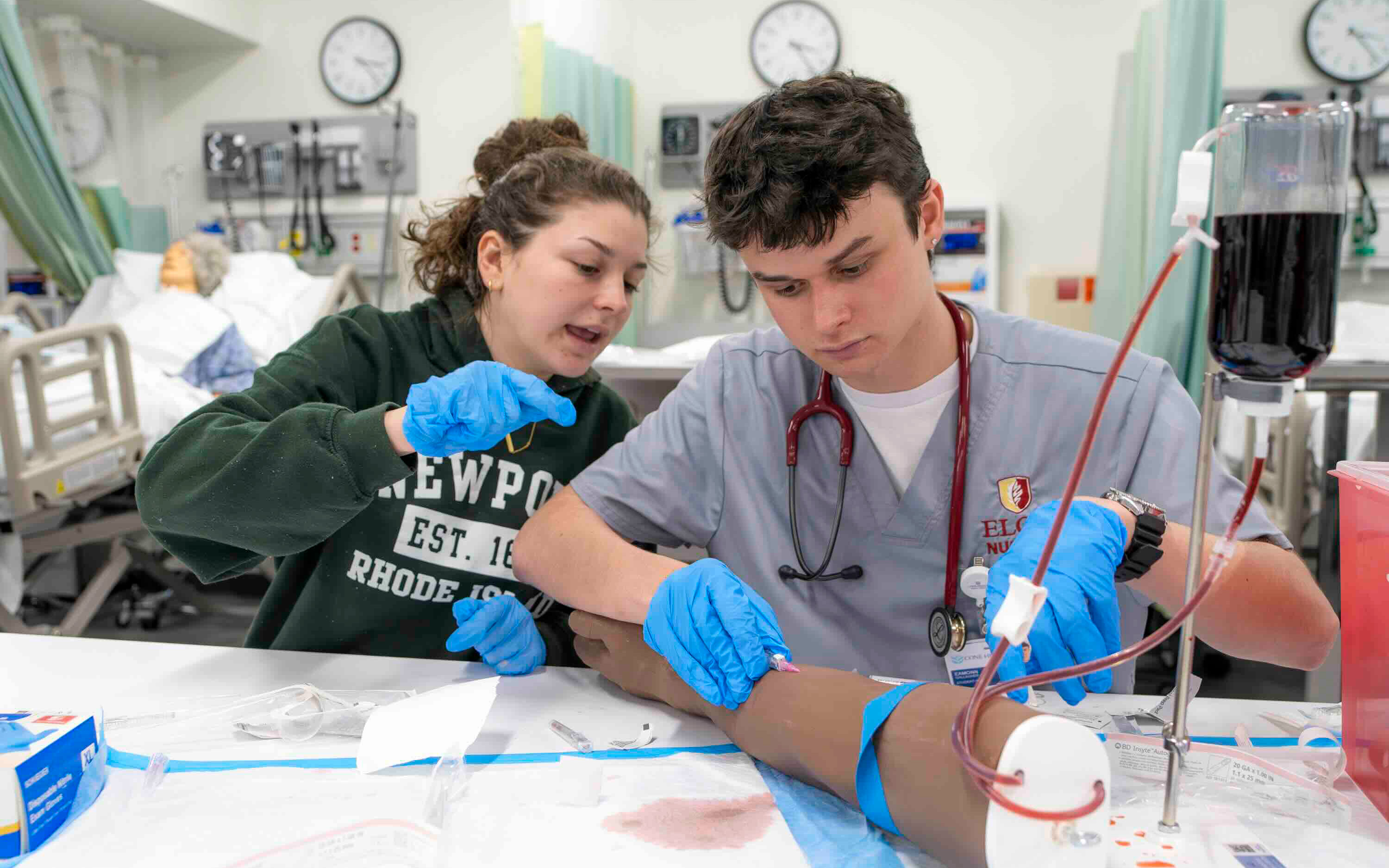 Two students work on inserting an IV in a mannequin arm.
