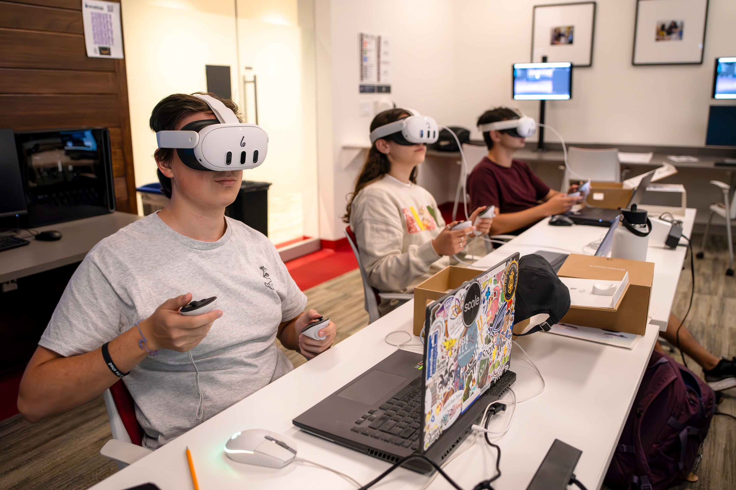 Three students work with VR goggles in a computer science classroom.