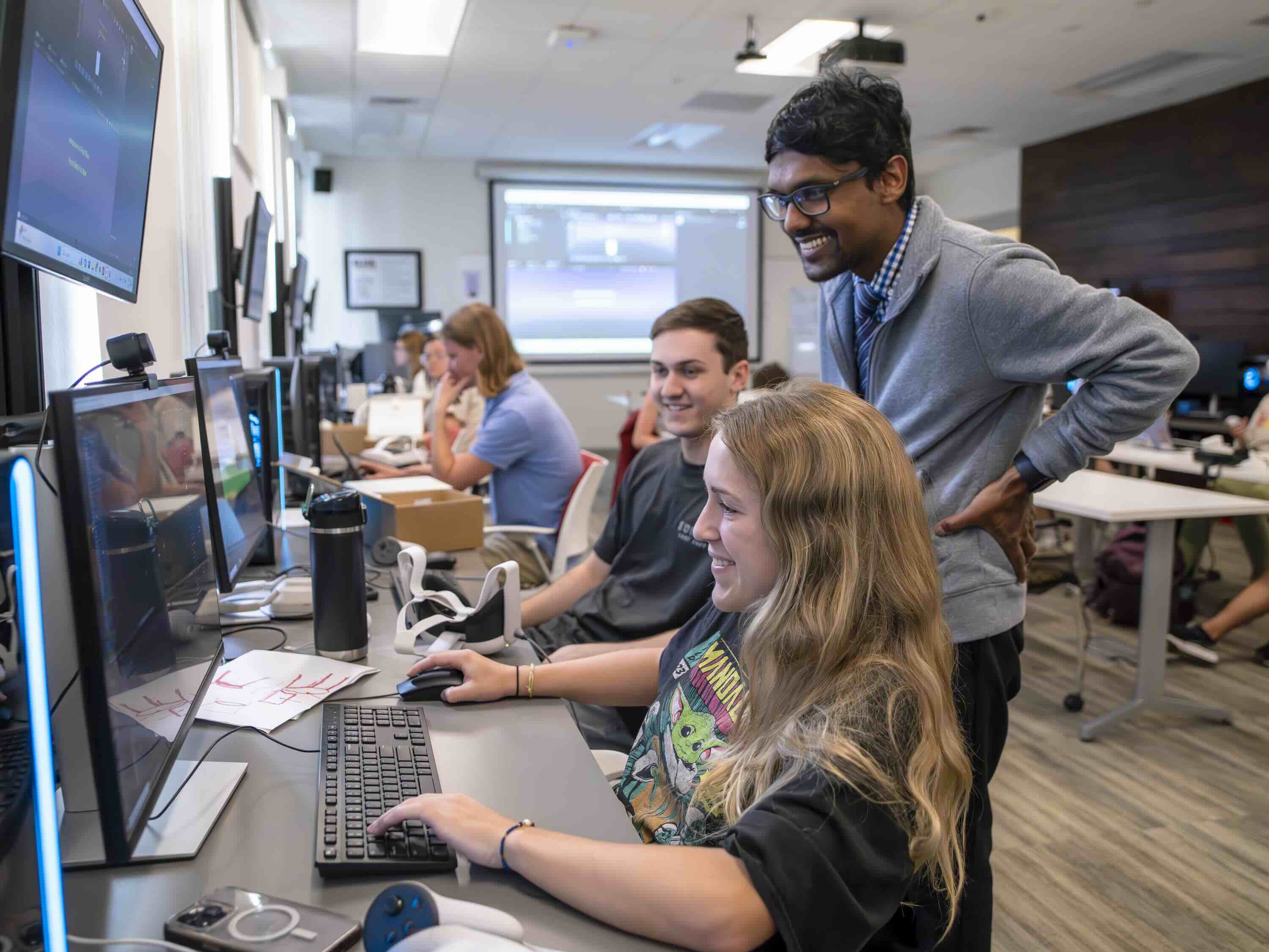 A professor watches a student editing a game design in a computer science class.