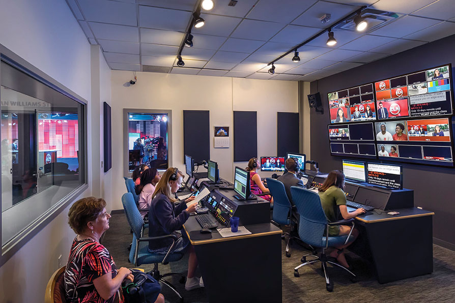 Students sit in front of monitors in a communications control room.