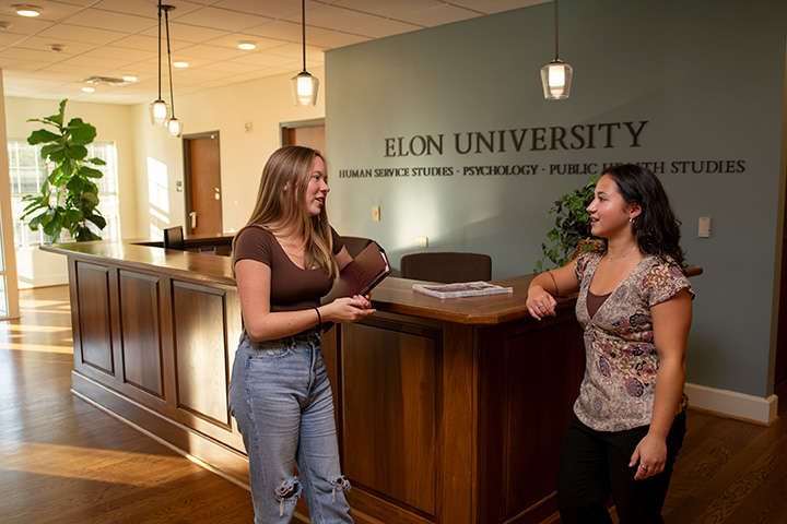 Two people stand at a reception desk in the building that houses human service studies, psychology and public health studies.