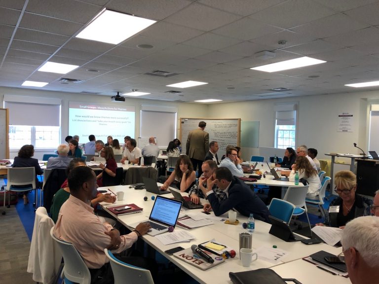 Students, faculty and staff on the Strategic Planning Committee gather around tables in a meeting room during the June 2019 retreat.