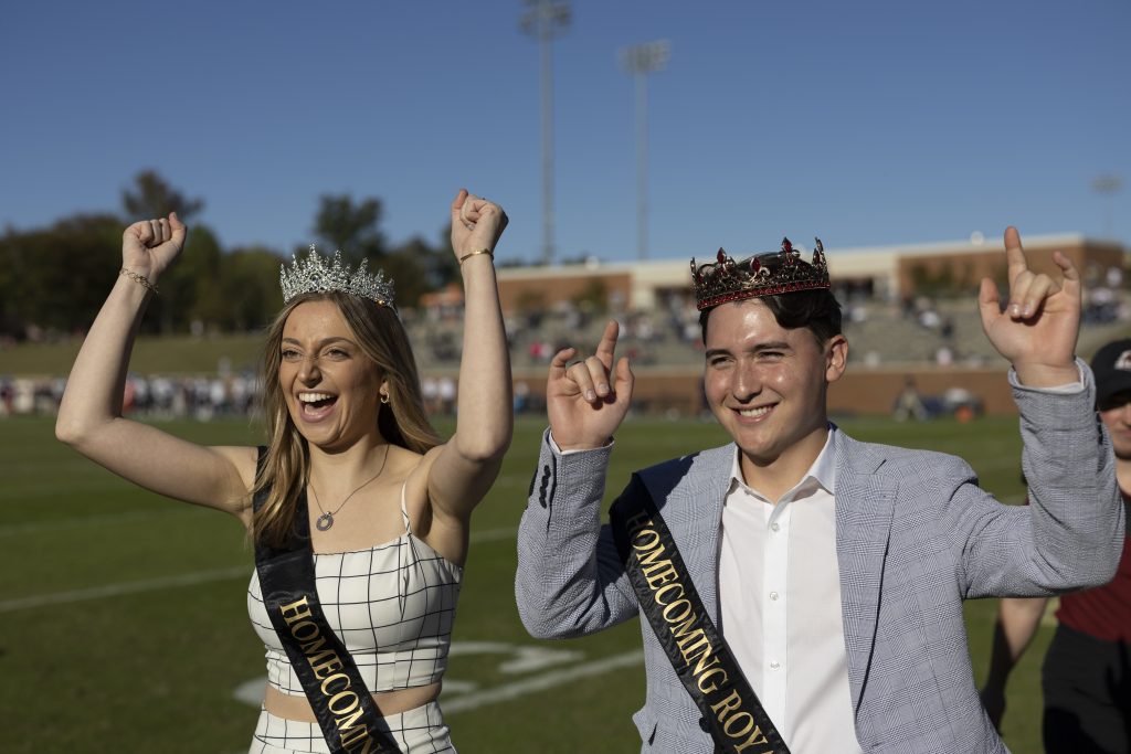 Two students with crowns and sashes on the field at Rhodes Stadium as Homecoming Royalty