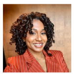 Profile photo of a women in an orange jacket in front of a brown back drop